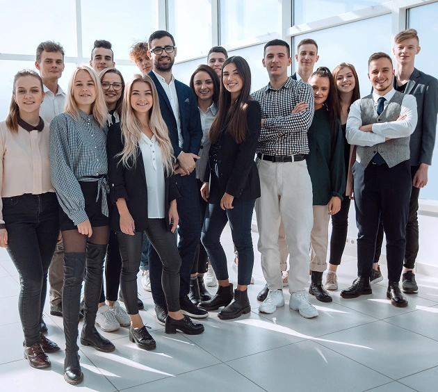 Een groep van 16 jonge professionals staat in een helder verlicht kantoor en glimlacht zelfverzekerd. Ze zijn gekleed in business-casual kleding, wat een gevoel van teamgeest en positiviteit uitstraalt.
