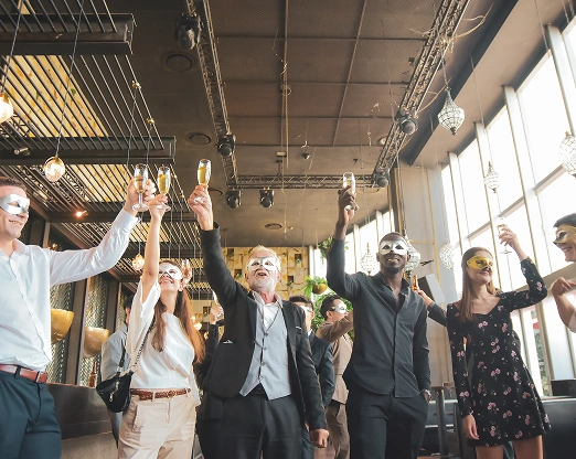 Een groep mensen met carnavalsmaskers proost met champagne in een stijlvolle, moderne ruimte. Onder de warme verlichting stralen ze vreugde en feestelijkheid uit.