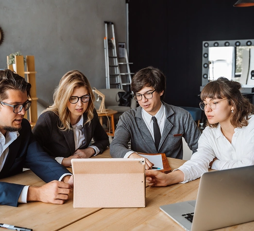 Een groep van vier professionals in zakelijke kleding kijkt aandachtig naar een tablet in een modern kantoor, wat een beeld schept van samenwerking en teamwork.